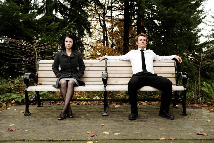 fall scene of a girl and guy sitting on opposite sides of a park bench, looking off in different directions