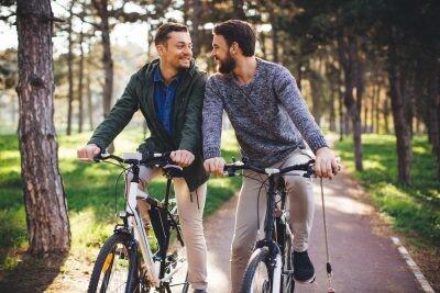 Beautiful gay couple at sunny day riding bike at park. They took a break to rest. Autumn sunny day.