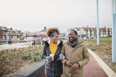 A couple walking arm-in-arm catching up over a coffee as they walk along a footpath. dating