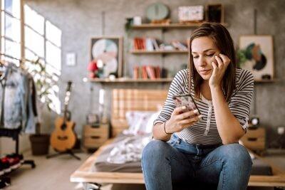 Beautiful young woman sitting on bed and chatting on social media