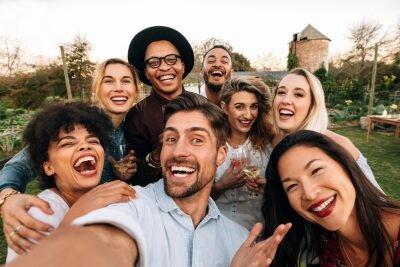 Friends chilling outside taking group photos and smiling. Laughing young people standing together outdoors and taking selfie.