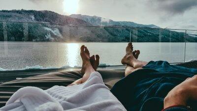 Couple relaxing on the sun beds in Spa of romance, Badehaus Millstätter See, Austria, by Millstätter See. Only the legs are visible and some parts of bathrobes. Snowy mountains in the back, snow on the terrace