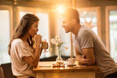 Young woman drinking coffee and communicating with her smiling boyfriend in a cafe.