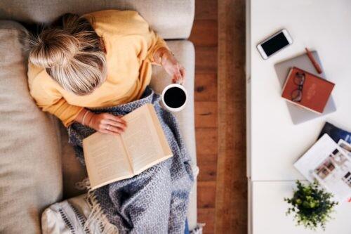 Overhead Shot Looking Down On Woman At Home Lying On Reading Book And Drinking Coffee for self-care