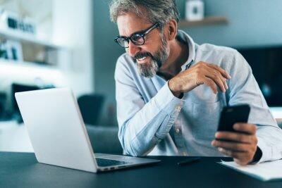 Mature businessman working at home using lap top and smart phone. matchmaker