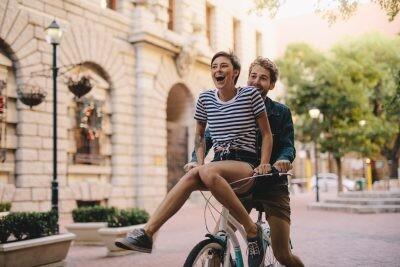 Couple enjoying on a bicycle in the city. Cheerful woman sitting on handlebar of boyfriends bicycle.