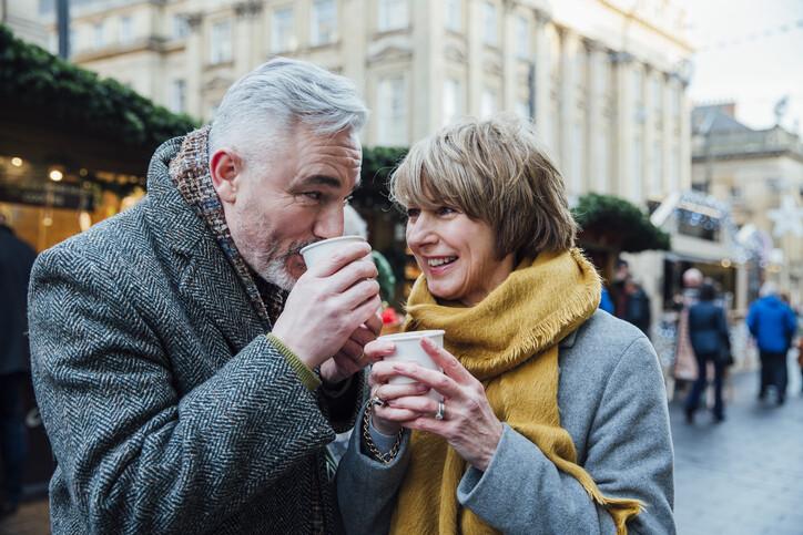 Mature couple are drinking hot drinks in a town christmas market dating