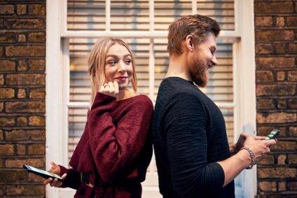 Shot of a young man and woman standing back to back and using their smartphones