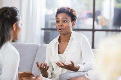Young African American woman gestures while talking with a female therapist. The patient has a concerned expression on her face with her dating coach