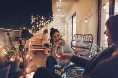 Young smiling woman enjoying in good wine and great company on the open terrace of her loft apartment