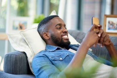 Shot of a young man using a cellphone while relaxing at home texting