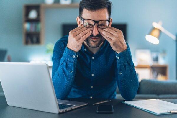 Tired young businessman working at home using lap top and looking Anxious, needs to invest time