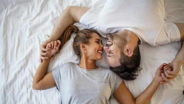 Guy and a girl in a cozy home environment. Happy man and woman lying in the bedroom stock photo. Top view of smiling young couple cuddling in bed in morning. Beautiful pair of lovers hug and kiss and happy