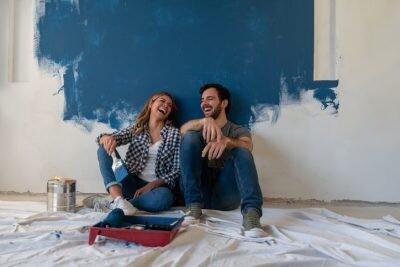 Portrait of a happy couple laughing while taking a break from painting - home improvement concepts in life
