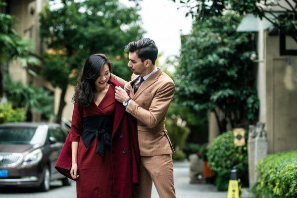 Handsome man helping his beautiful wife to dress up coat on the street, on beautiful day