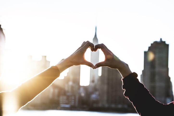 two people forming a heart shape with their hands, with the NYC skyline in the background